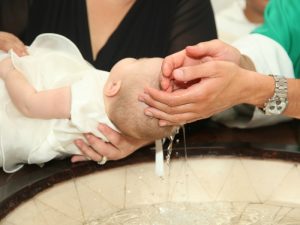 Newborn baby baptism by water with hands of priest